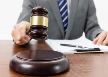 A closeup shot of a person with a gavel in hand and papers on the table
